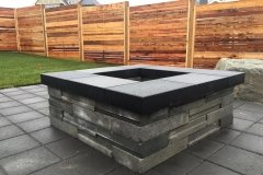 horizontal style fence with stone fire pit on a paving stone patio