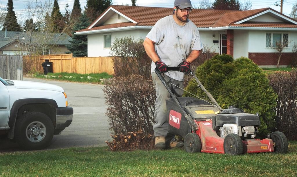 man in work clothes pushing lawn mower