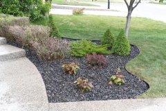assorted perennials in a bed with rundle rock and plastic edging