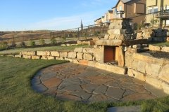 Stacked ironstone boulder retaining wall and outdoor fireplace with flagstone patio