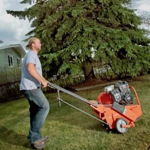 man pushing an aeration machine on lawn