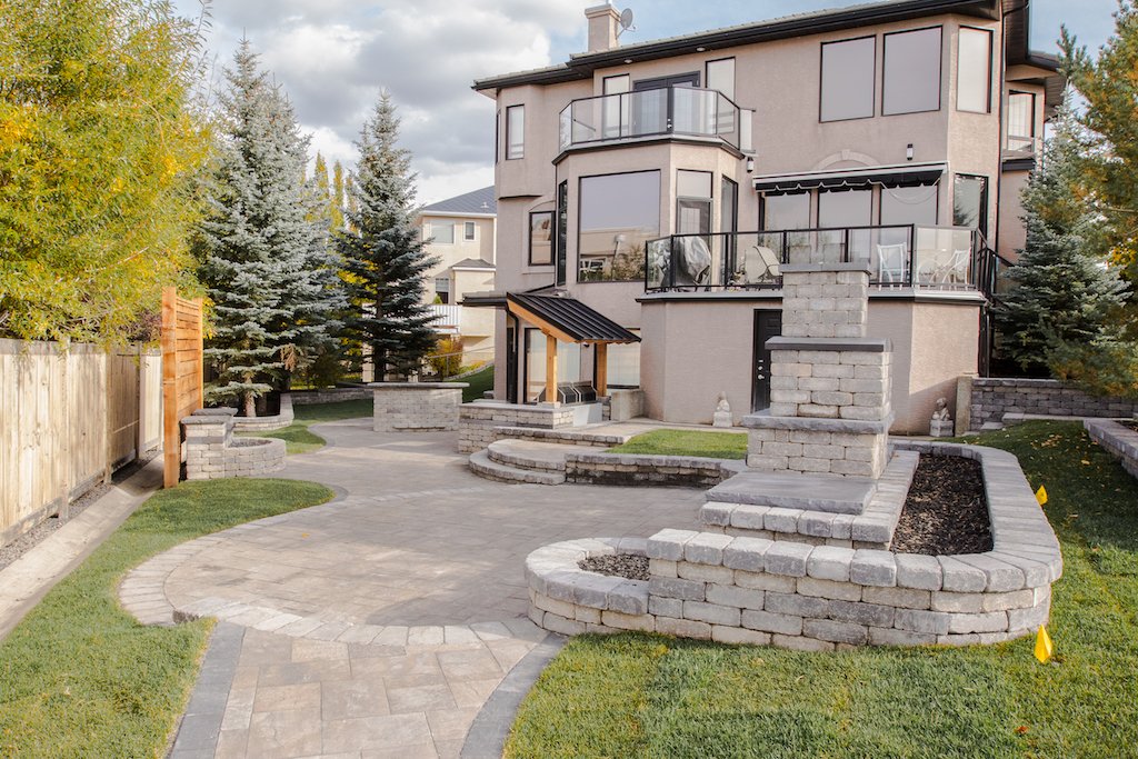 fully landscaped back yard with paving stone patio, raised stone bed and a stone fire place feature